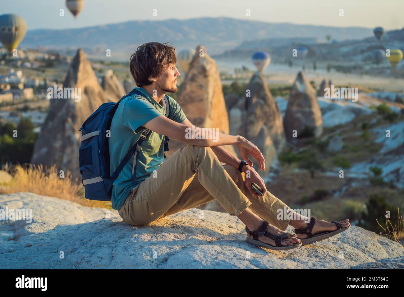 Turista che guarda mongolfiere in Cappadocia, Turchia. Buon viaggio in Turchia concetto. Uomo sulla cima di una montagna godendo di una vista meravigliosa Foto Stock