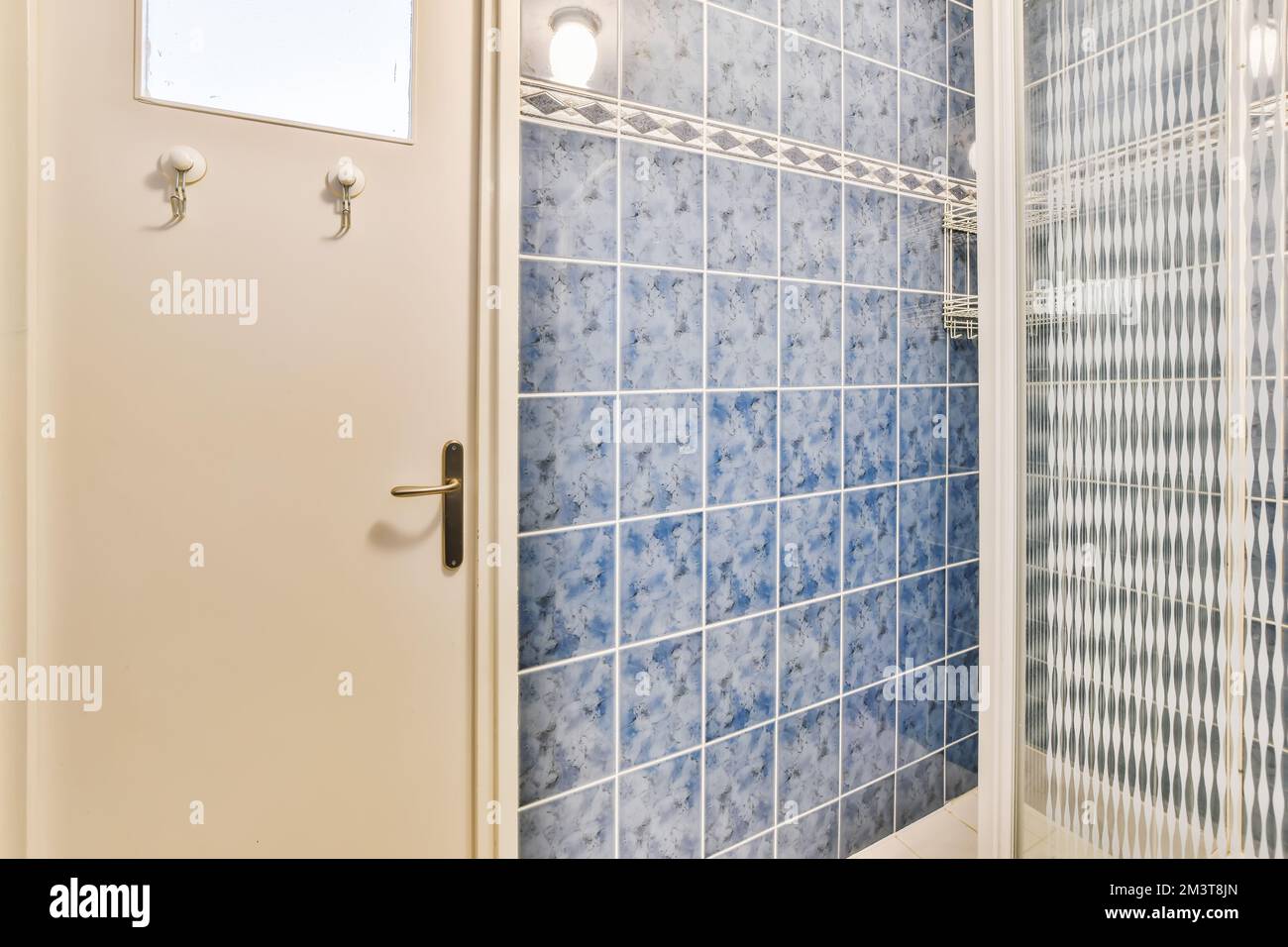 un bagno con piastrelle blu e bianche alle pareti, porta cabina doccia aperta per rivelare una cabina doccia Foto Stock