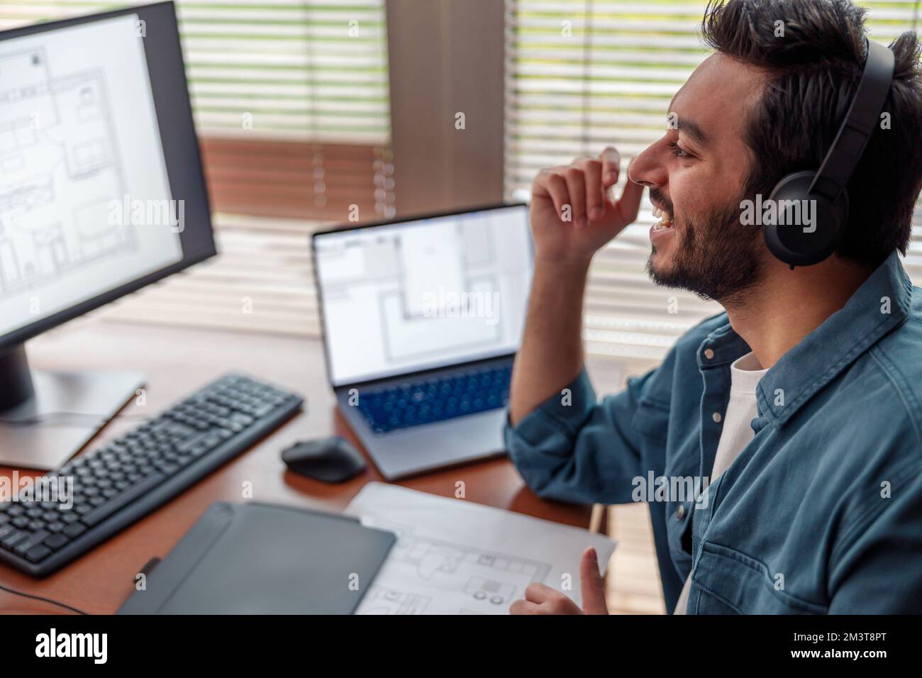 Sorridente uomo designer indiano in cuffie lavora in home Office disegno su tablet grafico Foto Stock