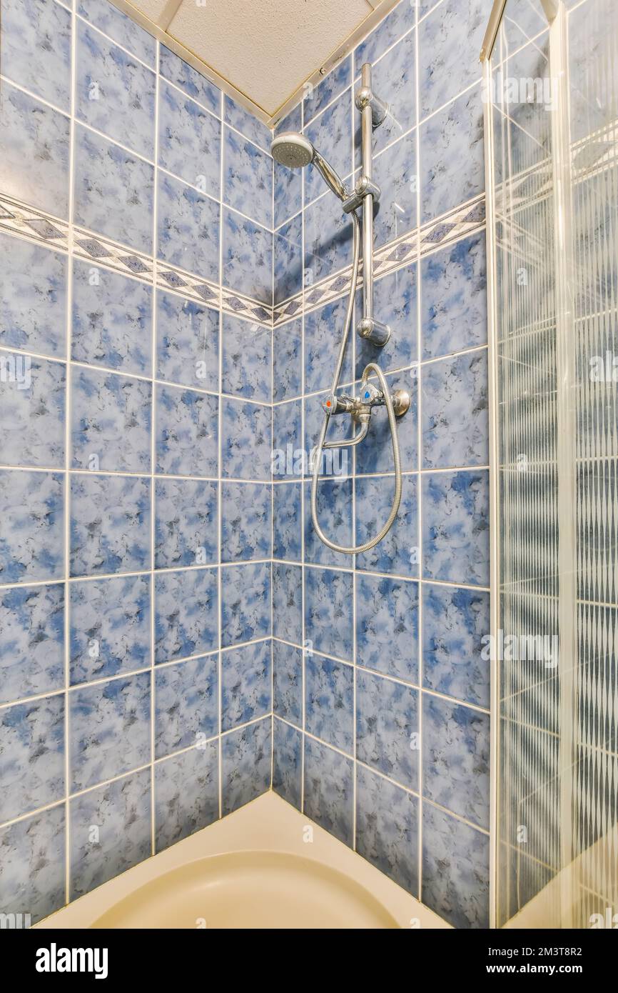 un bagno con piastrelle blu e bianche alle pareti, doccia con soffione nell'angolo accanto alla vasca Foto Stock