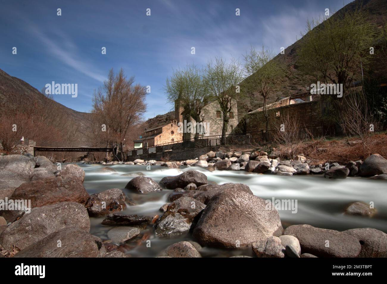 Un angolo basso di un fiume di montagna illuminato dal sole, erba gialla e pietre intorno Foto Stock