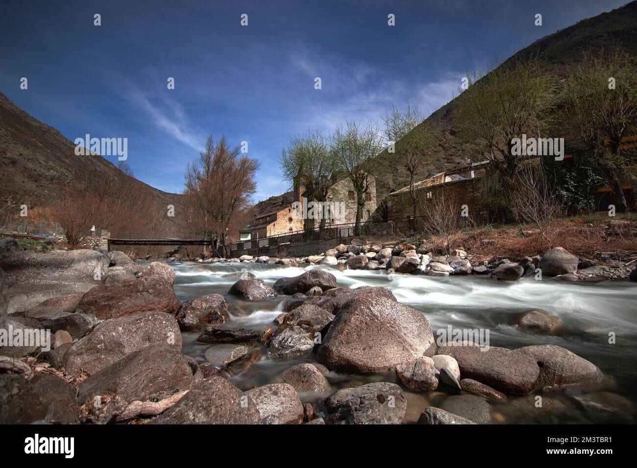 Un angolo basso di un fiume di montagna illuminato dal sole, erba gialla e pietre intorno Foto Stock