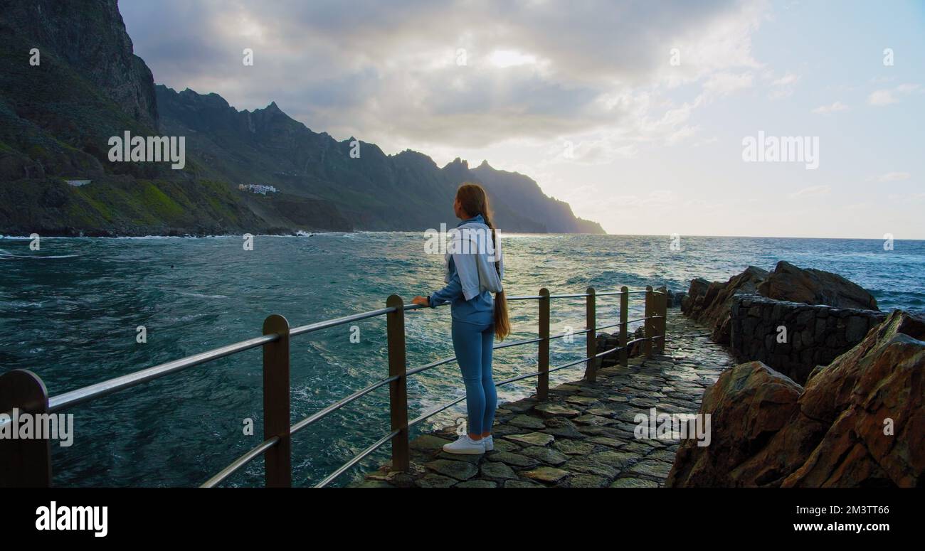 Donna che gode la vista del mare tempestoso al tramonto. Montagne vulcaniche di Anaga, isola delle Canarie, a nord di Tenerife. Splendidi paesaggi sul lungomare. Foto Stock