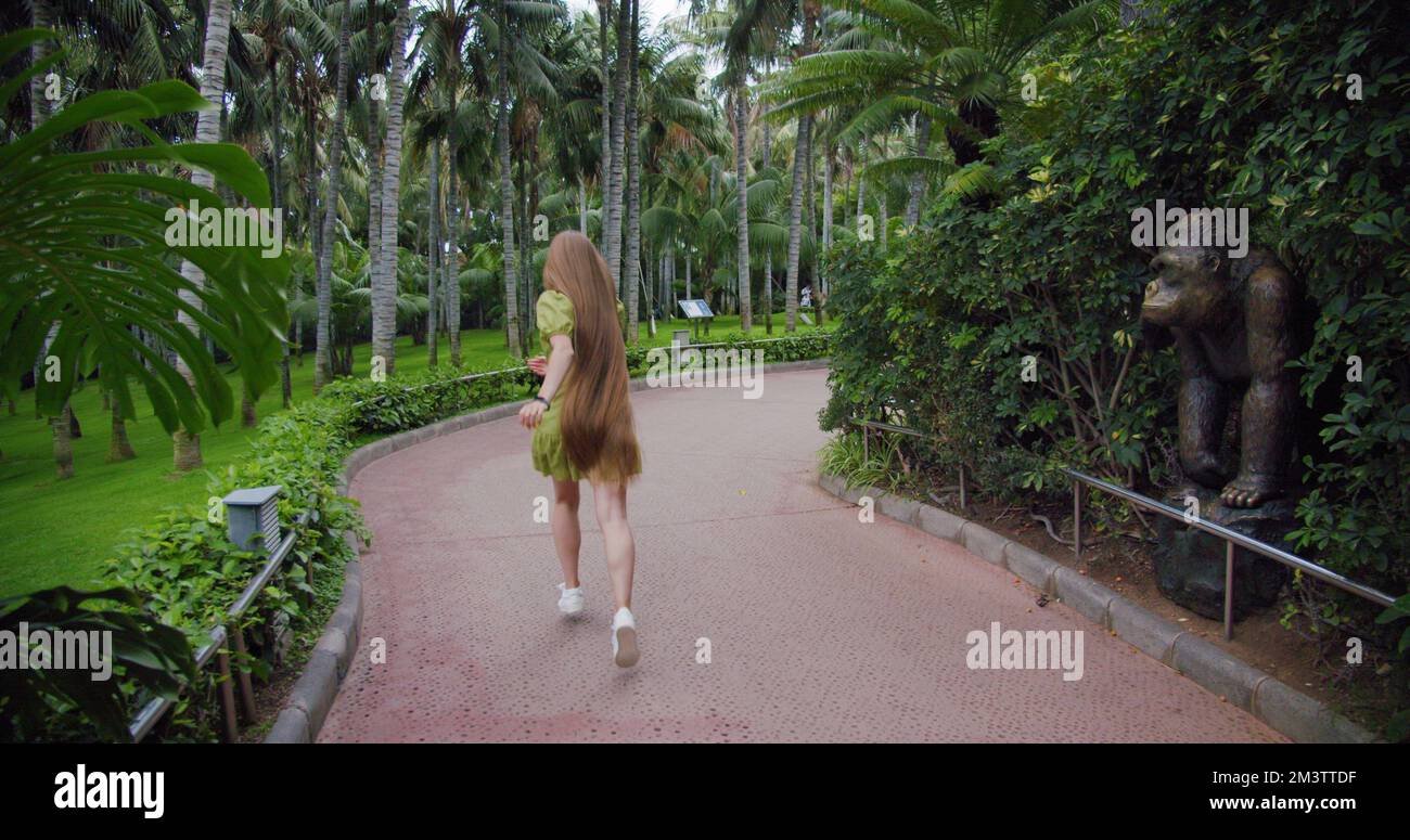 Silhouette di una donna felice che corre lungo la strada nel parco. Abito verde corto e capelli lunghi che soffiano nel vento. Foto Stock