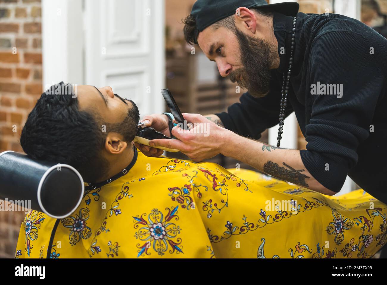 Barbiere focalizzato che taglia la barba del cliente in un barbiere. Il processo di styling di una barba. Foto di alta qualità Foto Stock