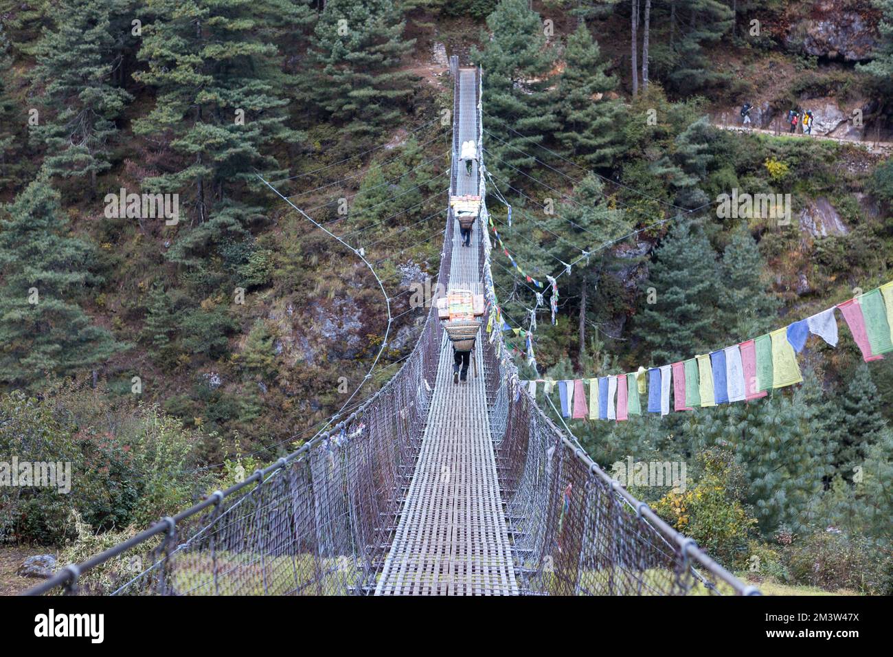 Everest base Camp Trek - 18 ottobre 2015: I portieri nepalesi trasportano merci sul ponte sospeso. Foto Stock