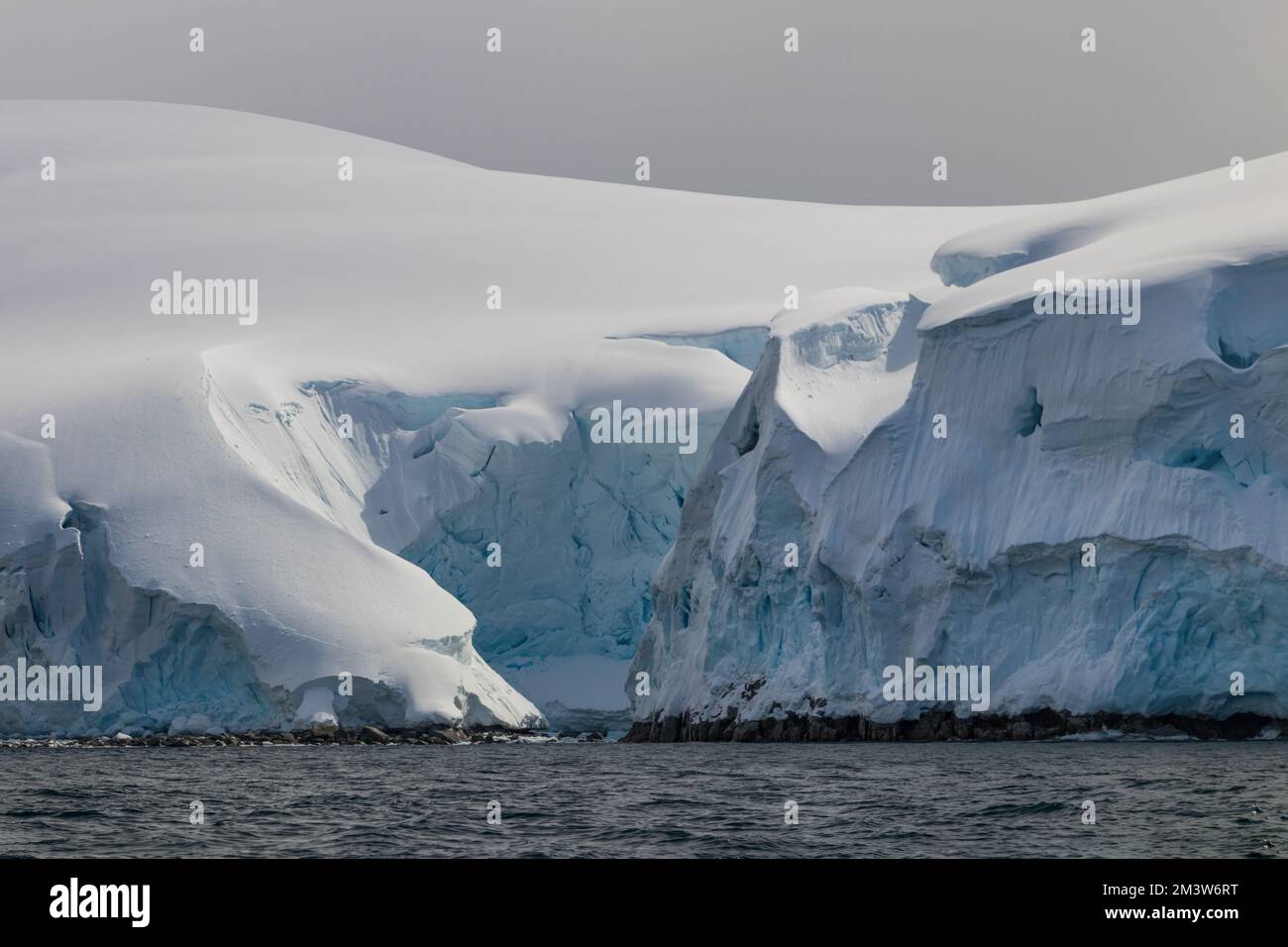 Vista in primo piano del bordo della penisola antartica, rivelando piccola insenatura. Rocce ricoperte di profondi strati di neve, ghiaccio blu e bianco. Foto Stock