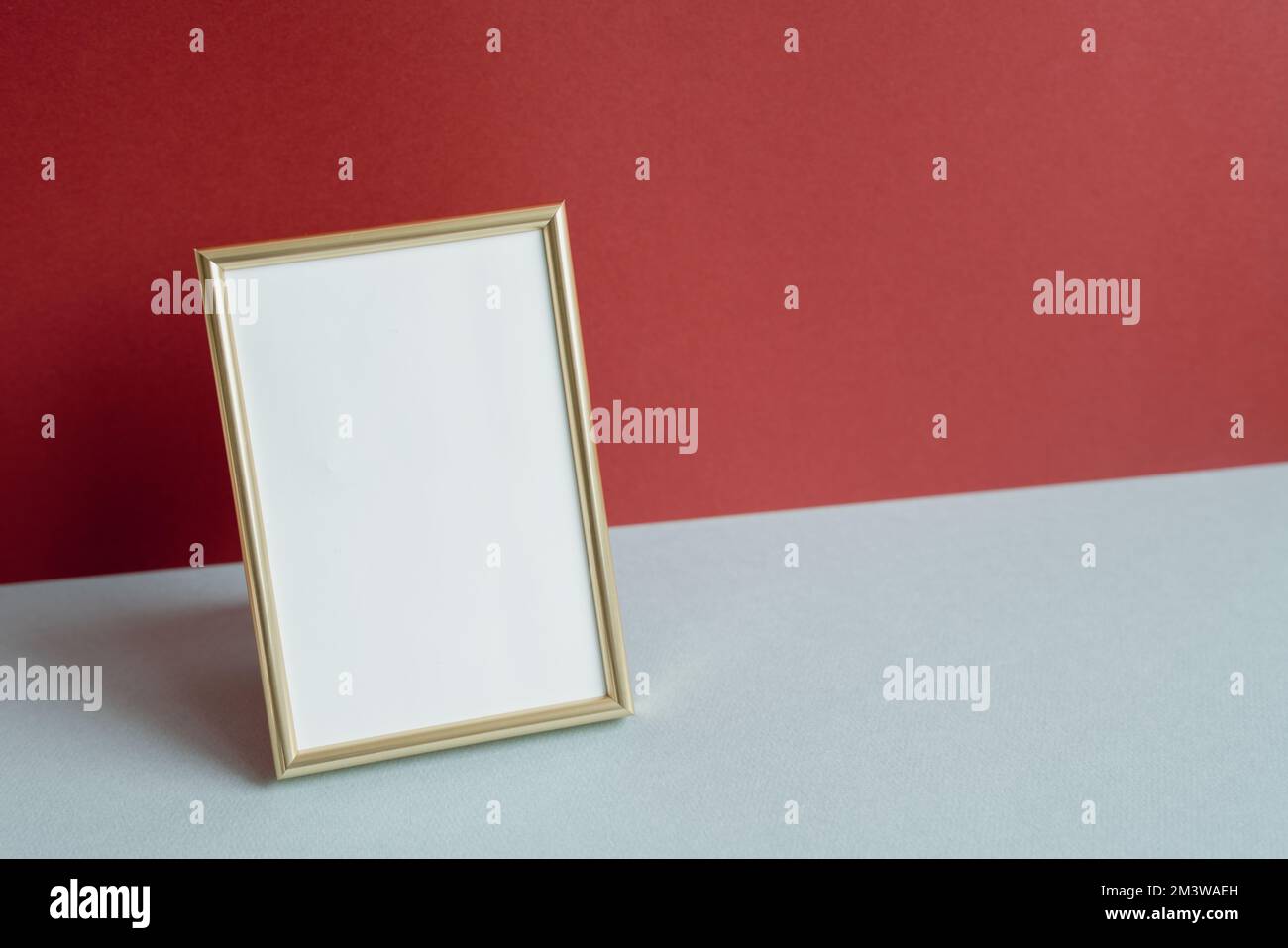 Cornice fotografica dorata con spazio vuoto bianco. biglietto di auguri. sfondo rosso e grigio Foto Stock