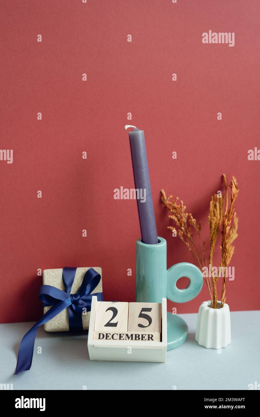 Confezione regalo d'oro, calendario in legno, candela, fiori secchi. Decorazioni natalizie. sfondo rosso e grigio. spazio di copia Foto Stock