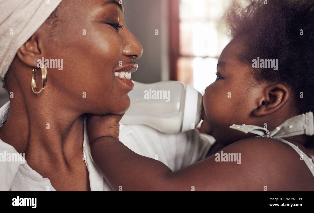 Hey là principessa graziosa. un'adorabile bambina che beve fuori dal biberon mentre si lega con la madre a casa. Foto Stock