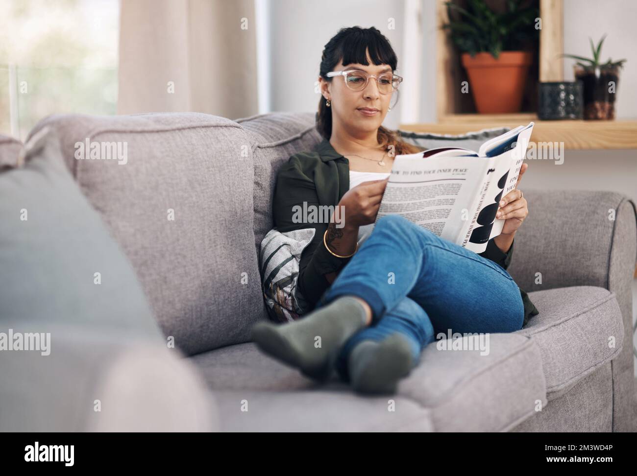 Questa trama è accattivante. Scatto a tutta lunghezza di una giovane donna attraente seduta da sola nel suo salotto e leggendo un libro. Foto Stock