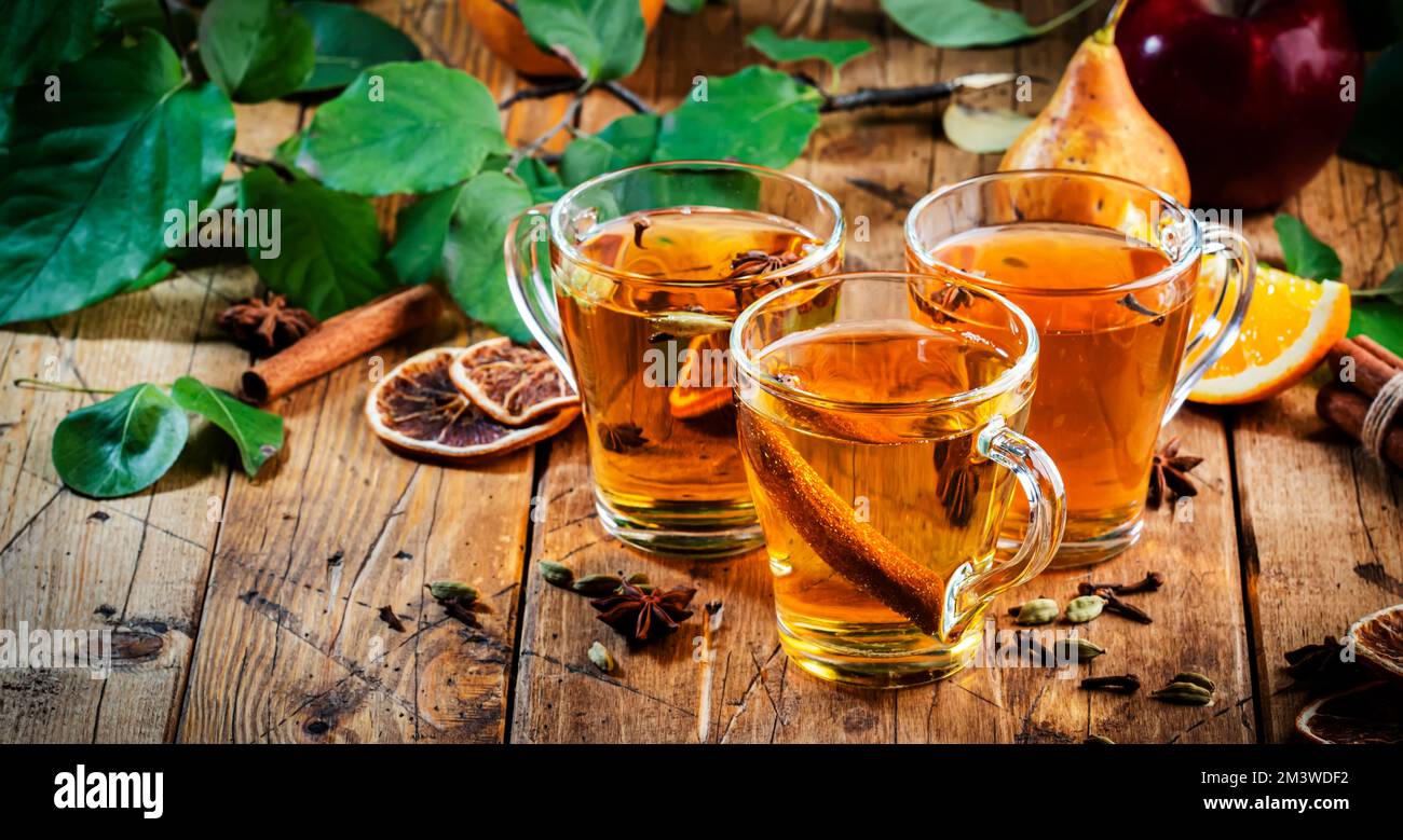 Bicchieri di sidro caldo in pacciamatura: mela, pera e arancia con spezie. Cocktail invernale fermentato a basso contenuto alcolico su un tavolo rustico in legno Foto Stock