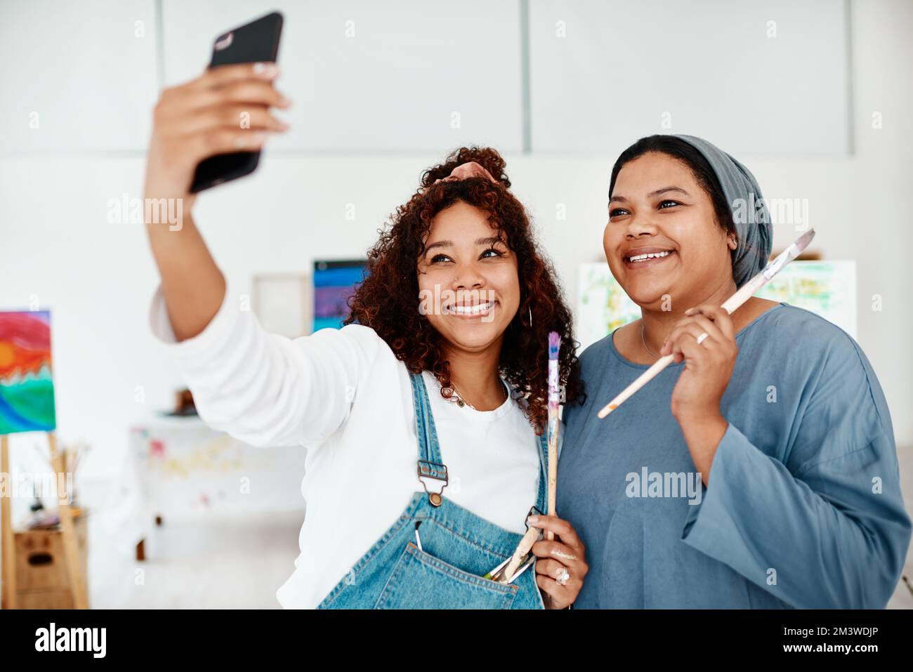 Raccogliere momenti, non cose. due giovani donne attraenti in piedi e utilizzando un cellulare per prendere un selfie durante una classe d'arte. Foto Stock