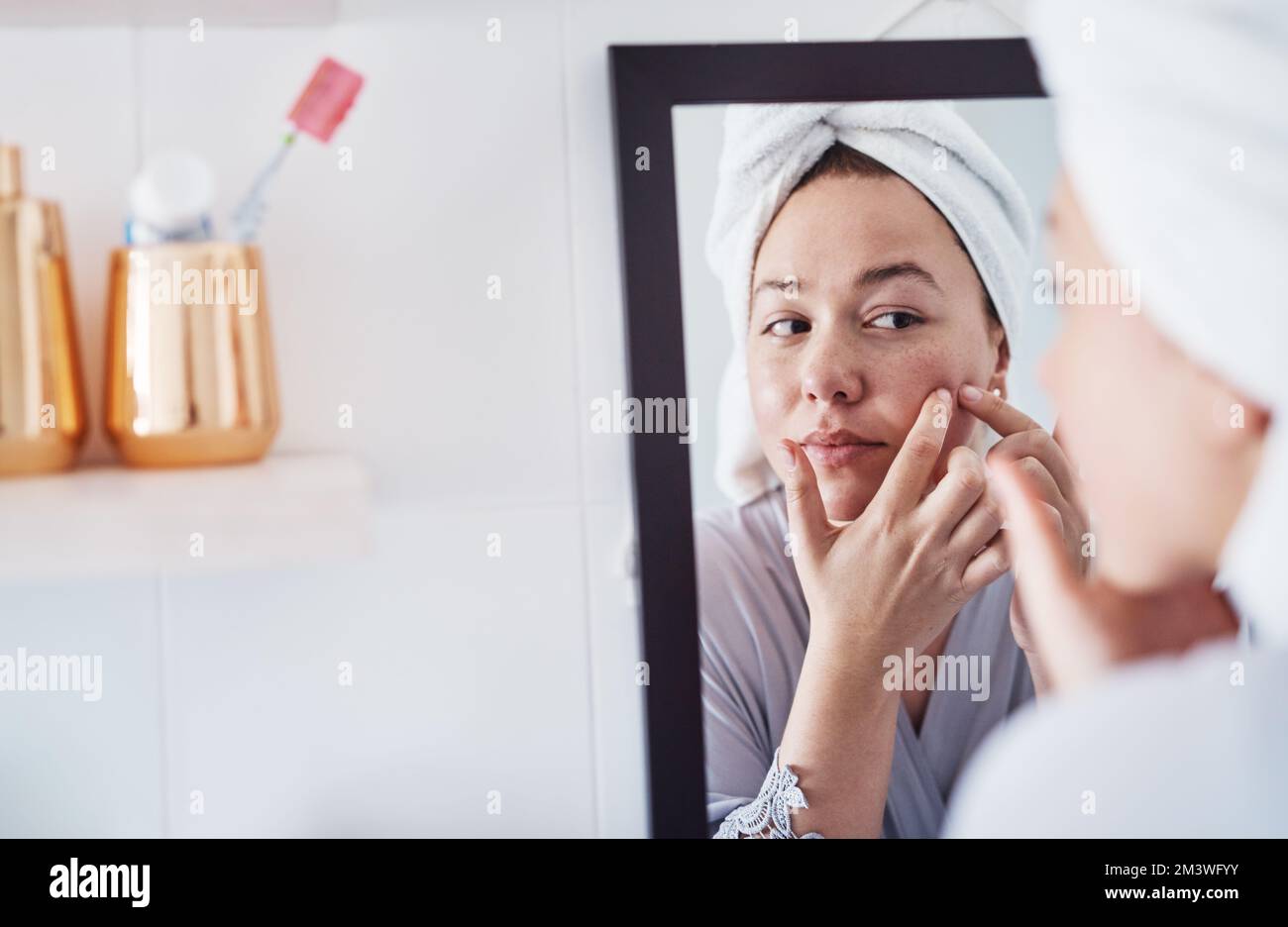 Schiacciare i pimples è genere di addictive. una bella giovane donna che analizza la sua pelle nello specchio del bagno. Foto Stock