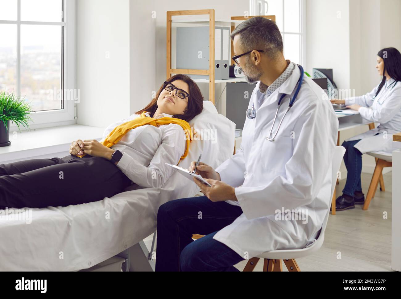La paziente si trova sul lettino di esame e ascolta il suo medico, che fa un piano per il suo trattamento. Foto Stock