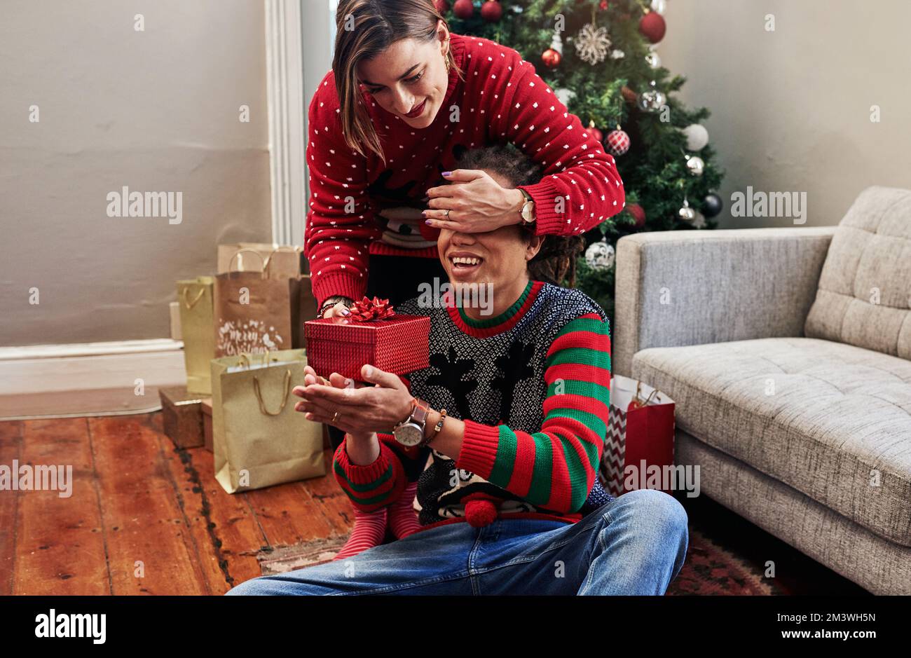 Okay, ora puoi quasi aprire gli occhi. una giovane donna allegra che tiene gli occhi dei mariti chiusi mentre dà a hime un regalo da aprire durante natale Foto Stock