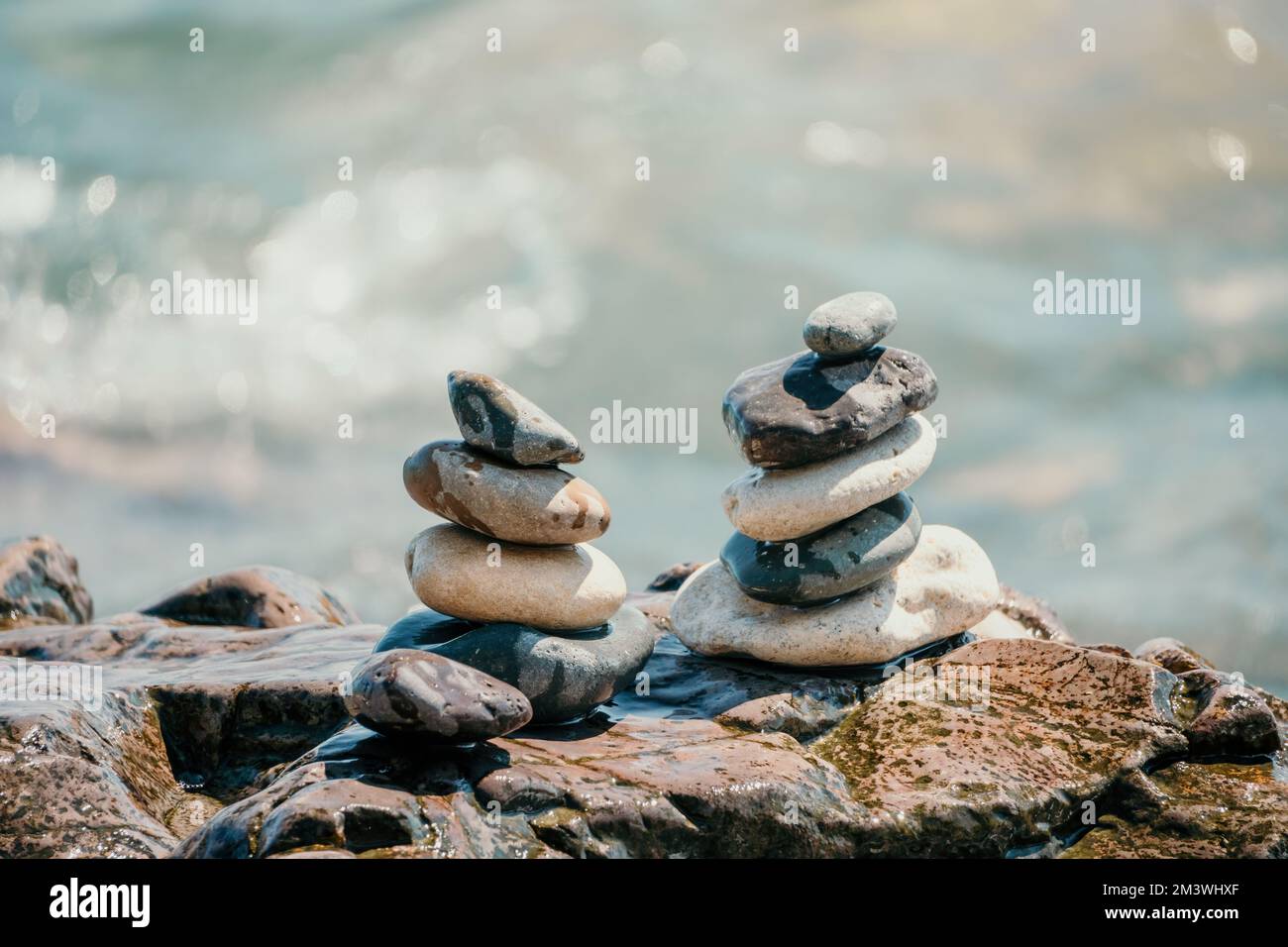 Piramide di roccia bilanciata sulla spiaggia di ciottoli, giorno di sole e cielo limpido al tramonto. Bokeh Golden Sea sullo sfondo. Fuoco selettivo, pietre zen sulla spiaggia di mare Foto Stock