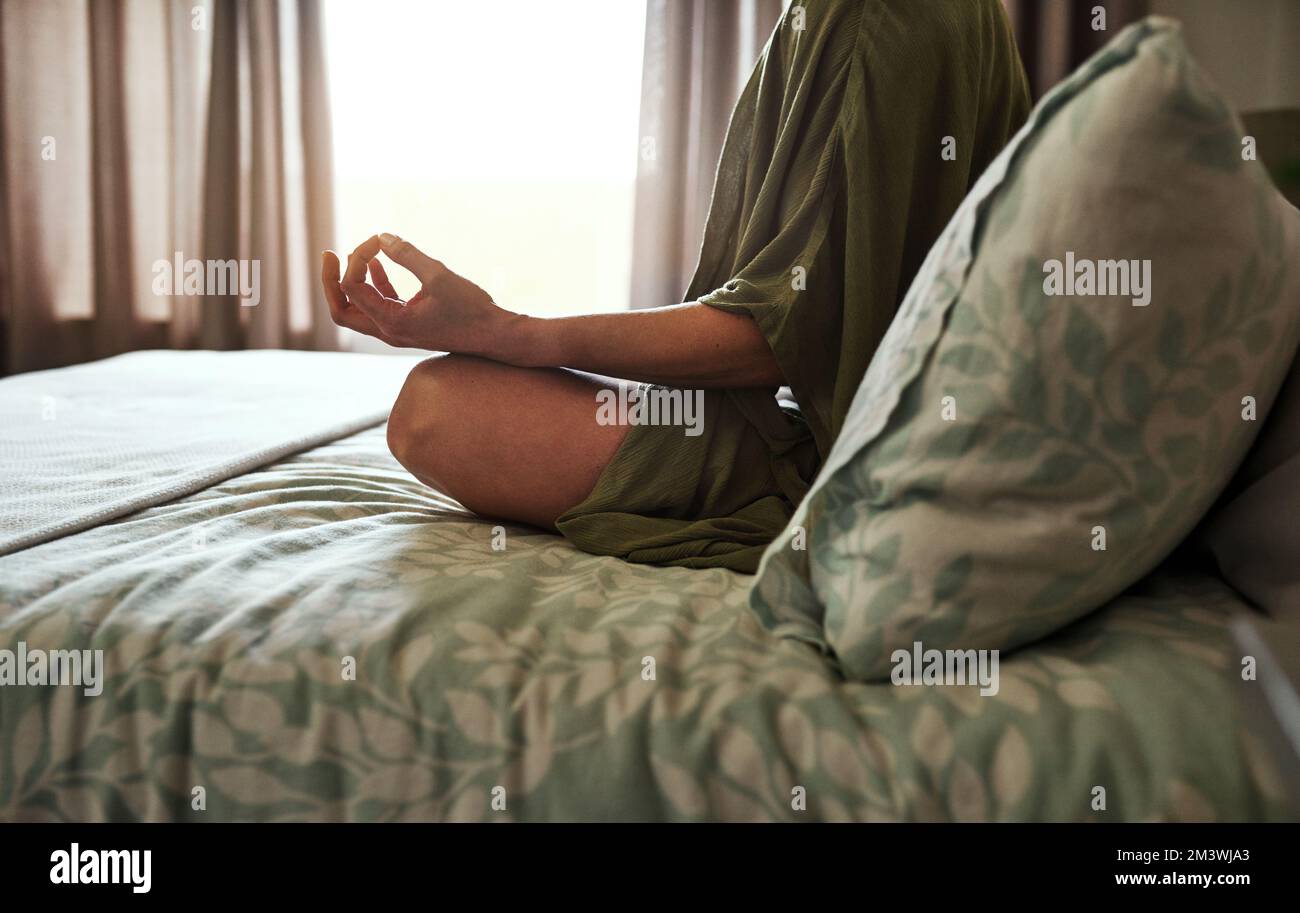 Lo yoga mette la mia mente a suo agio. una giovane donna irriconoscibile meditando mentre si siede sul suo letto a casa. Foto Stock