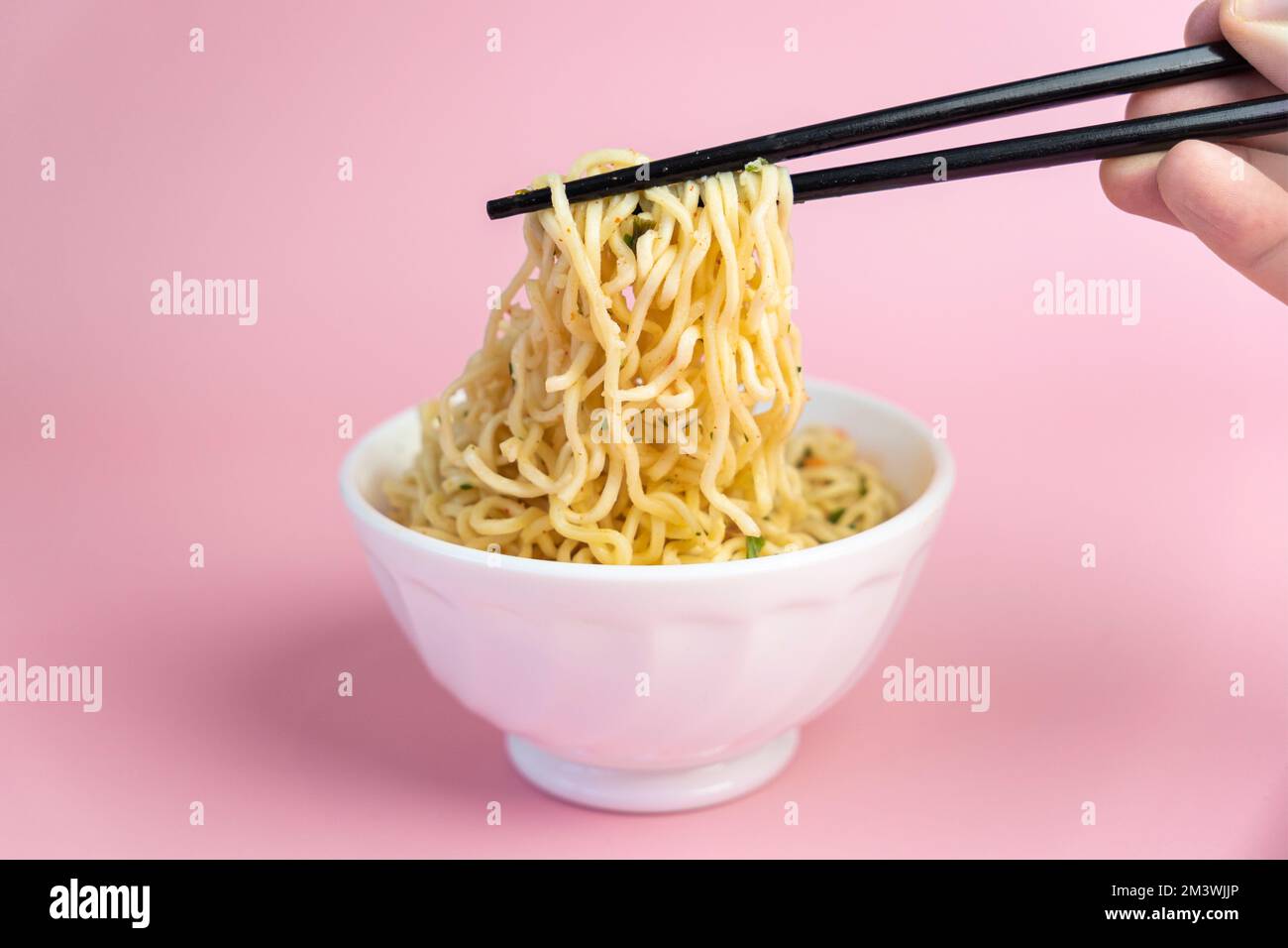 Ciotola bianca di tagliatelle su uno sfondo rosa, cibo veloce ed economico. Spaghetti cinesi istantanei. Cibo asiatico. Foto Stock