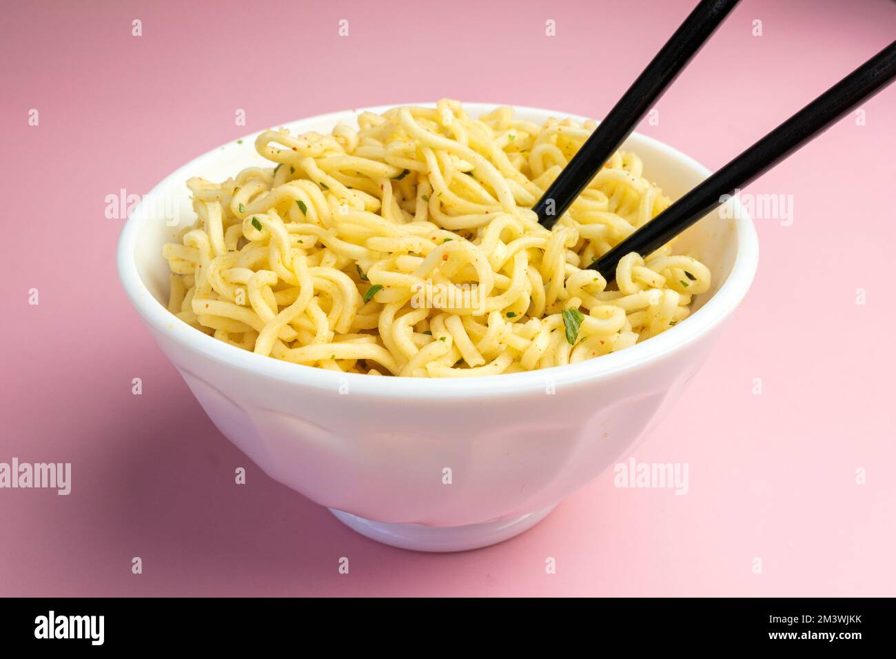 Ciotola bianca di tagliatelle su uno sfondo rosa, cibo veloce ed economico. Spaghetti cinesi istantanei. Cibo asiatico. Foto Stock