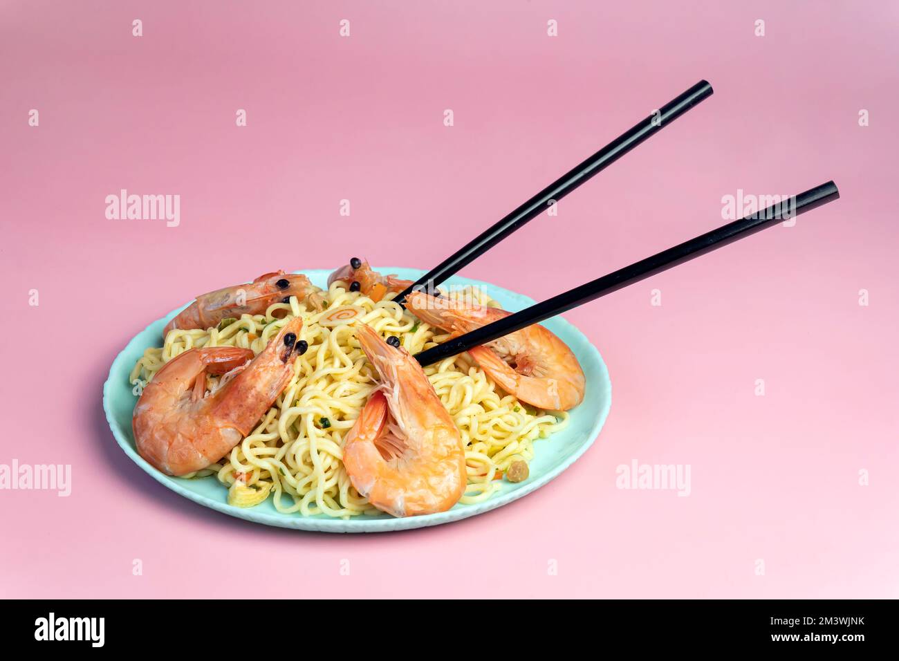 Spaghetti istantanei con gamberetti fritti, cipolle verdi su sfondo rosa brillante. Ricette rapide per la cucina estiva asiatica Foto Stock
