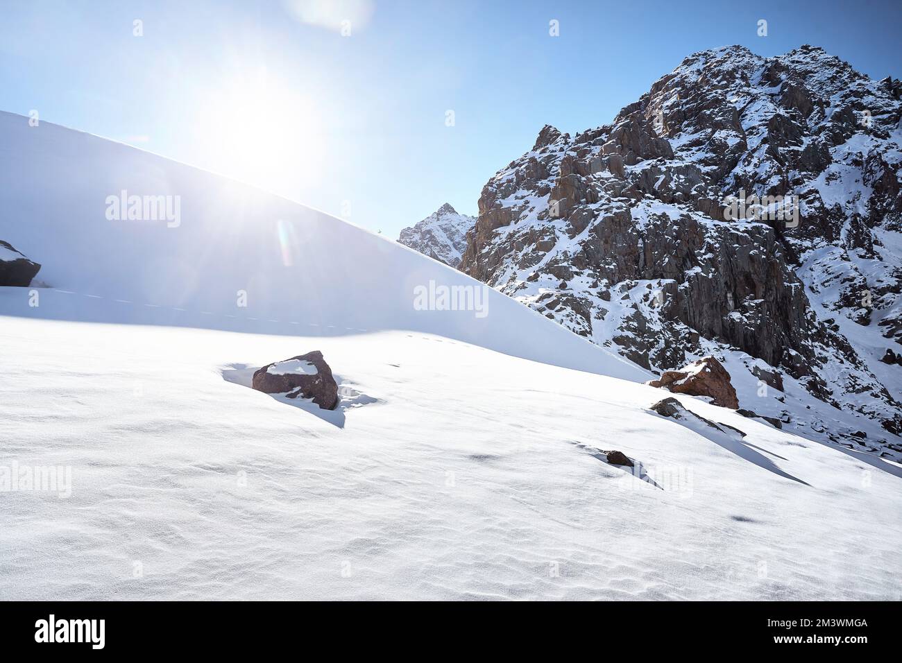 Giorno di sole sulle montagne di alta neve paesaggio con sole bagliore bagliore contro il cielo blu nel periodo invernale in Kazakistan Foto Stock