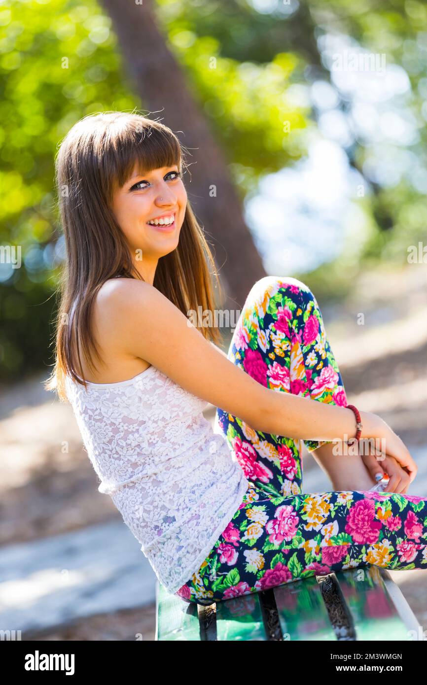Sorridente adolescente felice seduto su panca nel parco guardando la fotocamera occhio occhi contatto eyeshot Estate Summertime Foto Stock