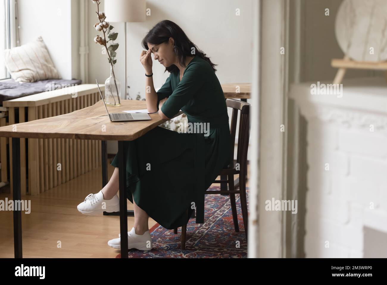 Donna stanca seduta a un tavolo con un computer portatile in ufficio a casa Foto Stock