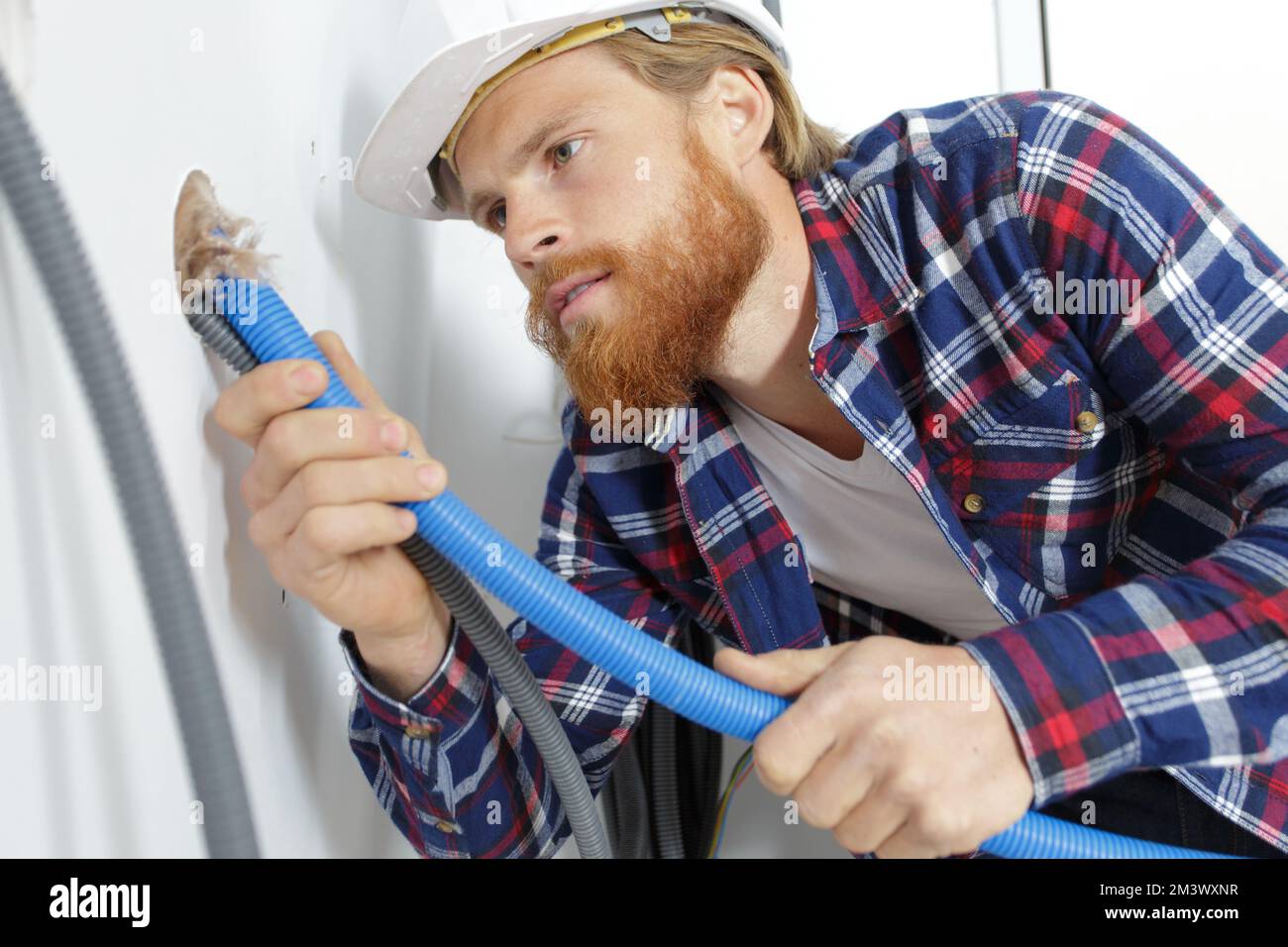costruttore maschio che passa il condotto del cavo nella parete Foto Stock