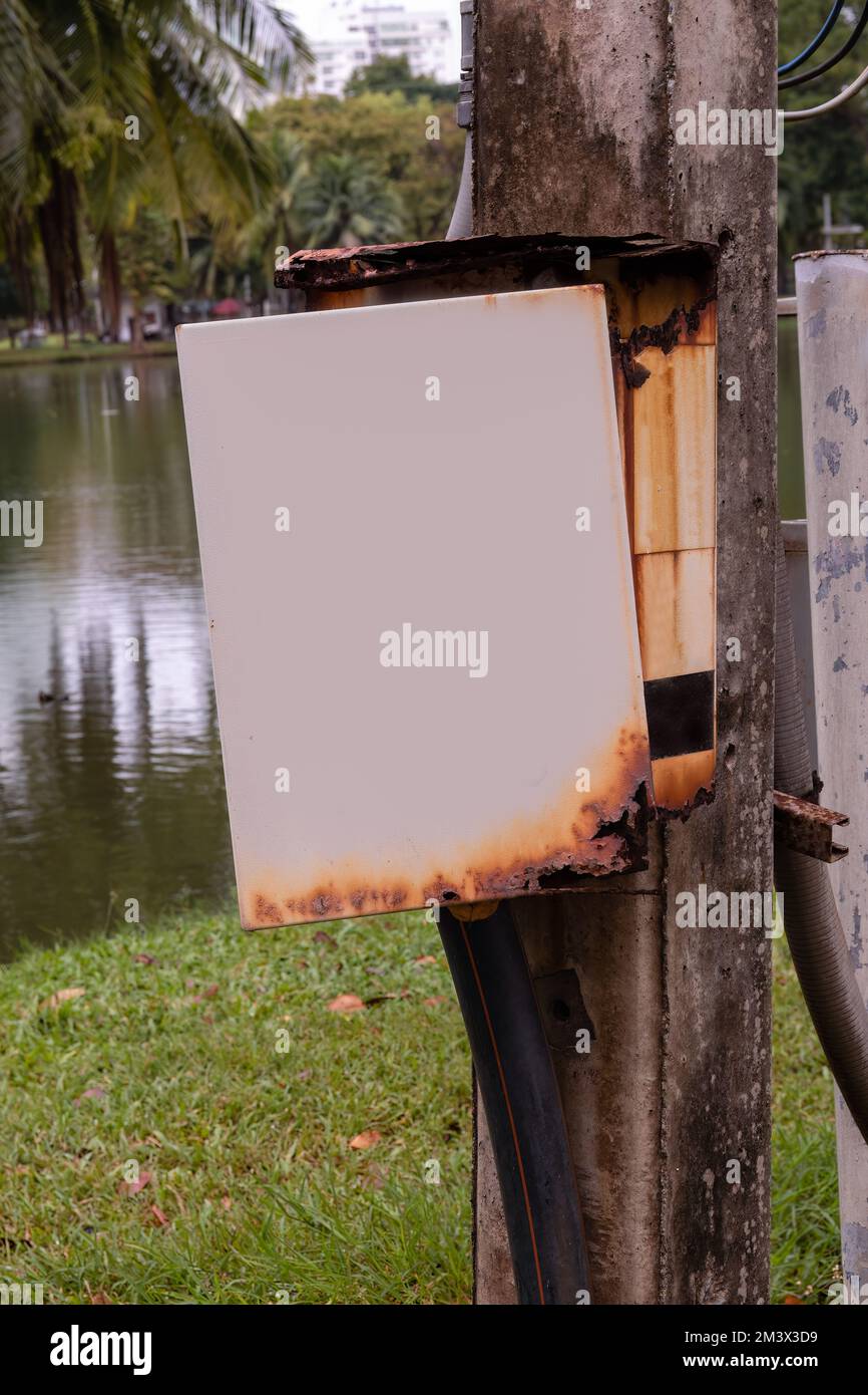Scatola elettrica arrugginita con una porta aperta accanto ad un lago in un parco Foto Stock