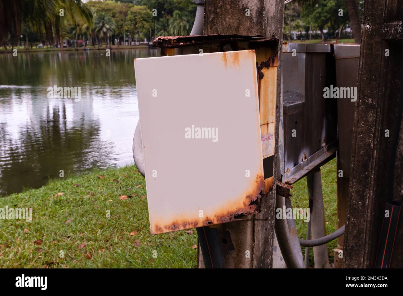 Scatola elettrica arrugginita con una porta aperta accanto ad un lago in un parco Foto Stock