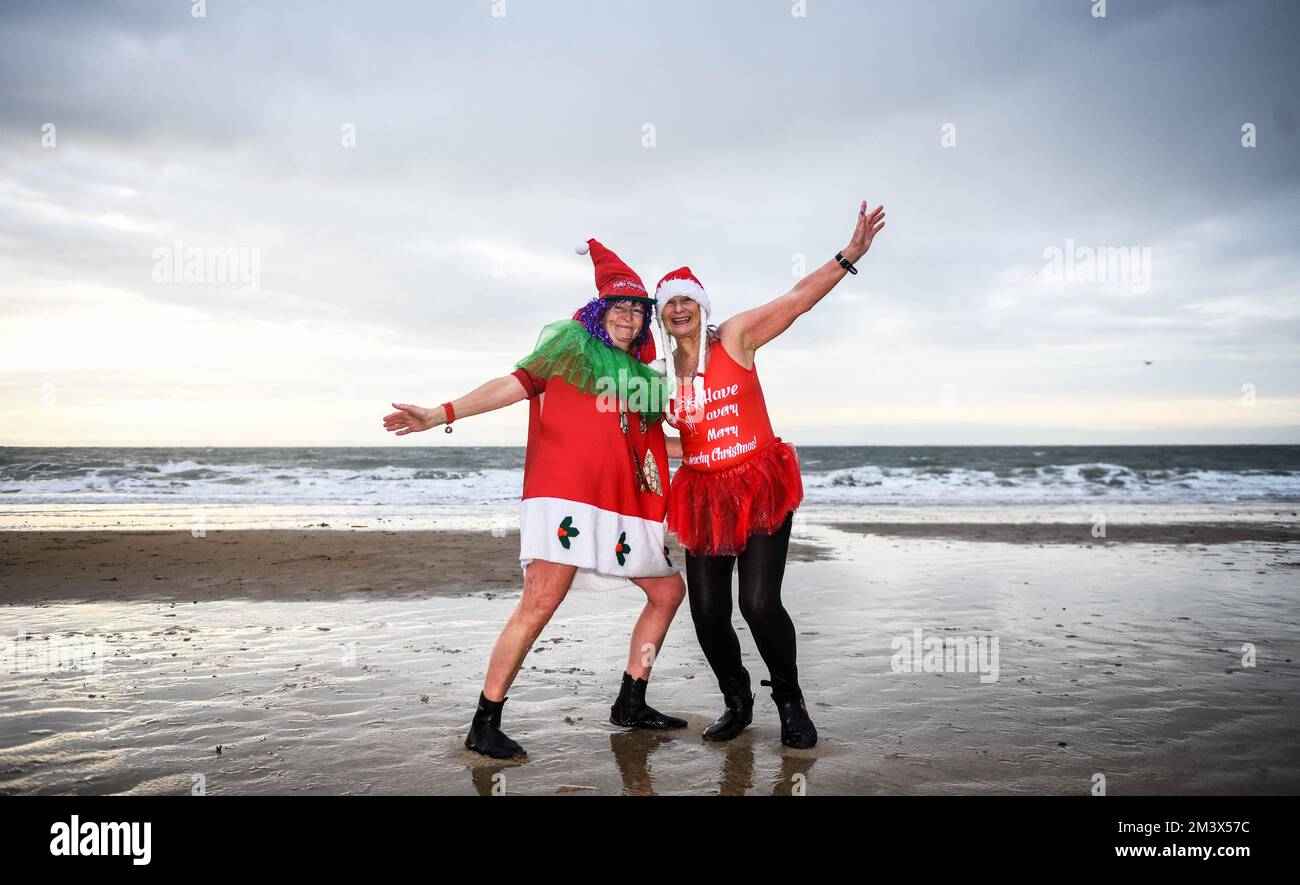 Fund Raisers, Sian Lewis e Faye Kinseler (a destra) vengono fotografati prima di dirigersi nelle acque ghiacciate di Langland Bay, Swansea durante l'evento annuale di Santa Surf che si svolge presso la spiaggia di Gower ogni anno per raccogliere fondi per i surfisti contro la fognatura e aiutare i surfisti locali a entrare nello spirito natalizio. Foto Stock