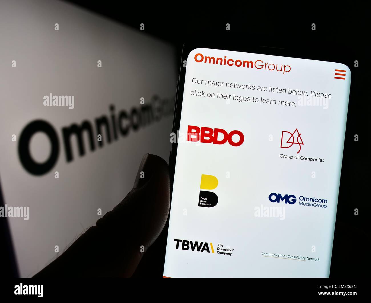 Persona che tiene il cellulare con il sito web della società di media statunitense Omnicom Group Inc. Sullo schermo di fronte al logo. Messa a fuoco al centro del display del telefono. Foto Stock