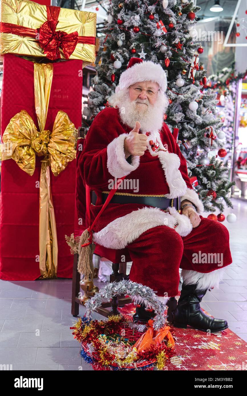 Babbo Natale presso l'albero di Natale seduto con grandi regali. Milano, Italia - Dicembre 2022 Foto Stock