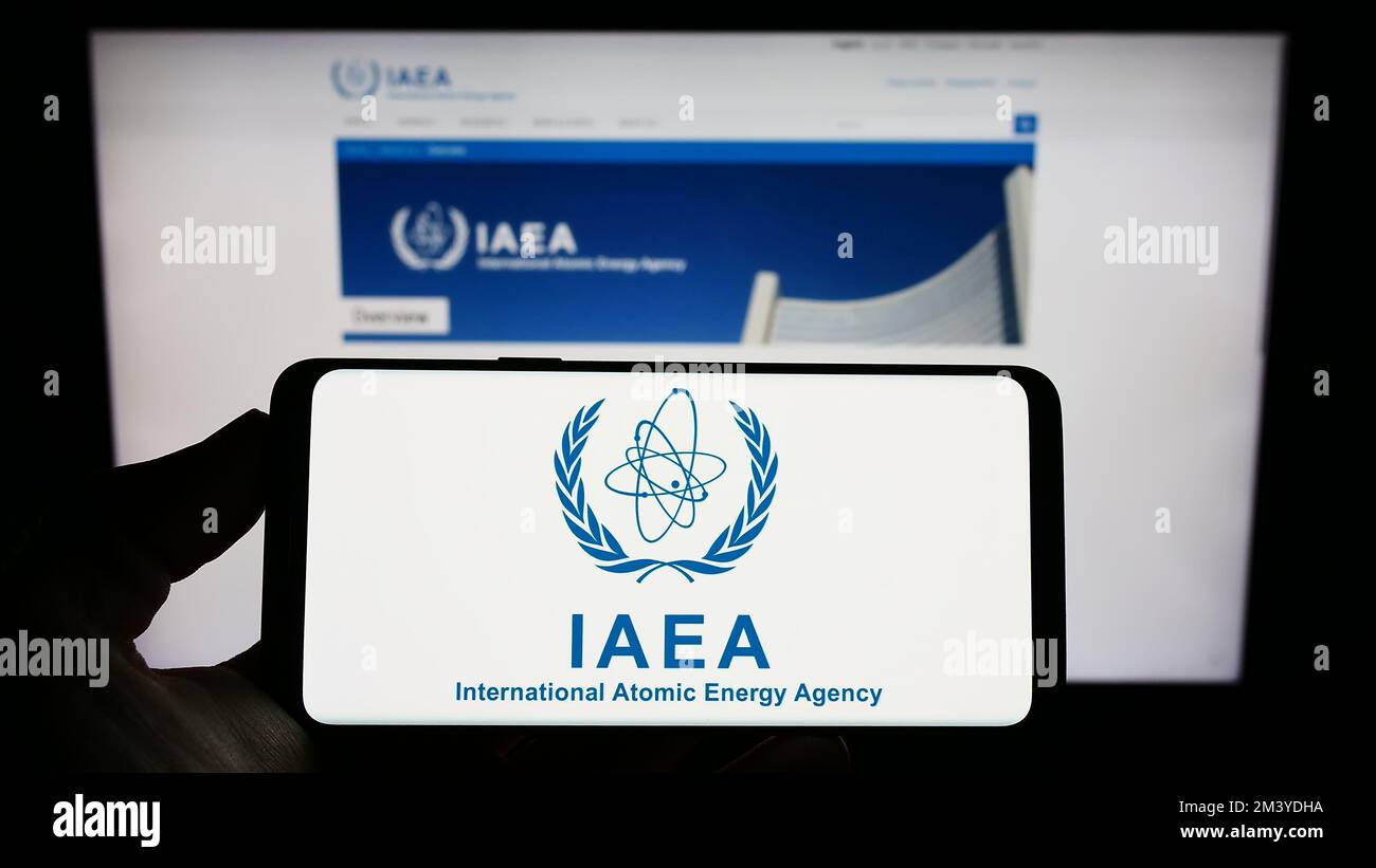Persona che tiene uno smartphone con il logo dell'Agenzia internazionale dell'energia atomica (AIEA) sullo schermo di fronte al sito Web. Messa a fuoco sul display del telefono. Foto Stock