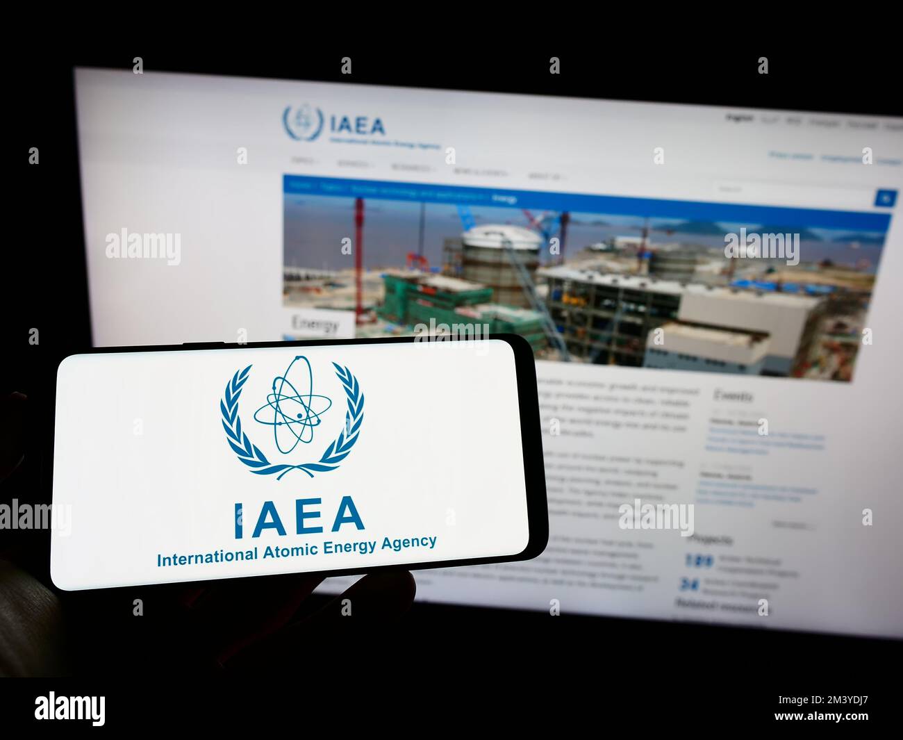 Persona che tiene il cellulare con il logo dell'Agenzia internazionale per l'energia atomica (AIEA) sullo schermo di fronte alla pagina web. Messa a fuoco sul display del telefono. Foto Stock