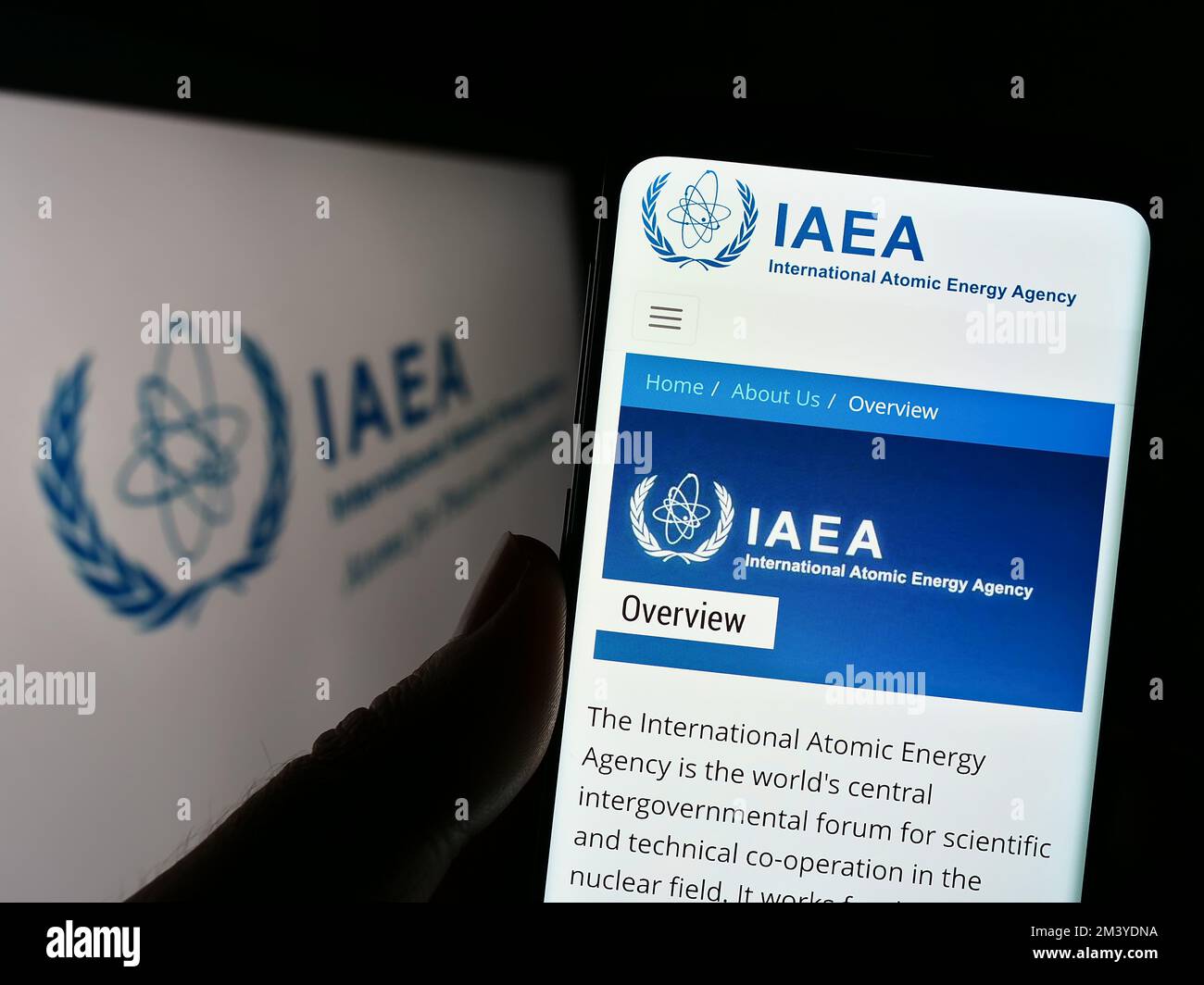 Persona che tiene un telefono cellulare con il sito web dell'Agenzia internazionale dell'energia atomica (AIEA) sullo schermo con il logo. Messa a fuoco al centro del display del telefono. Foto Stock