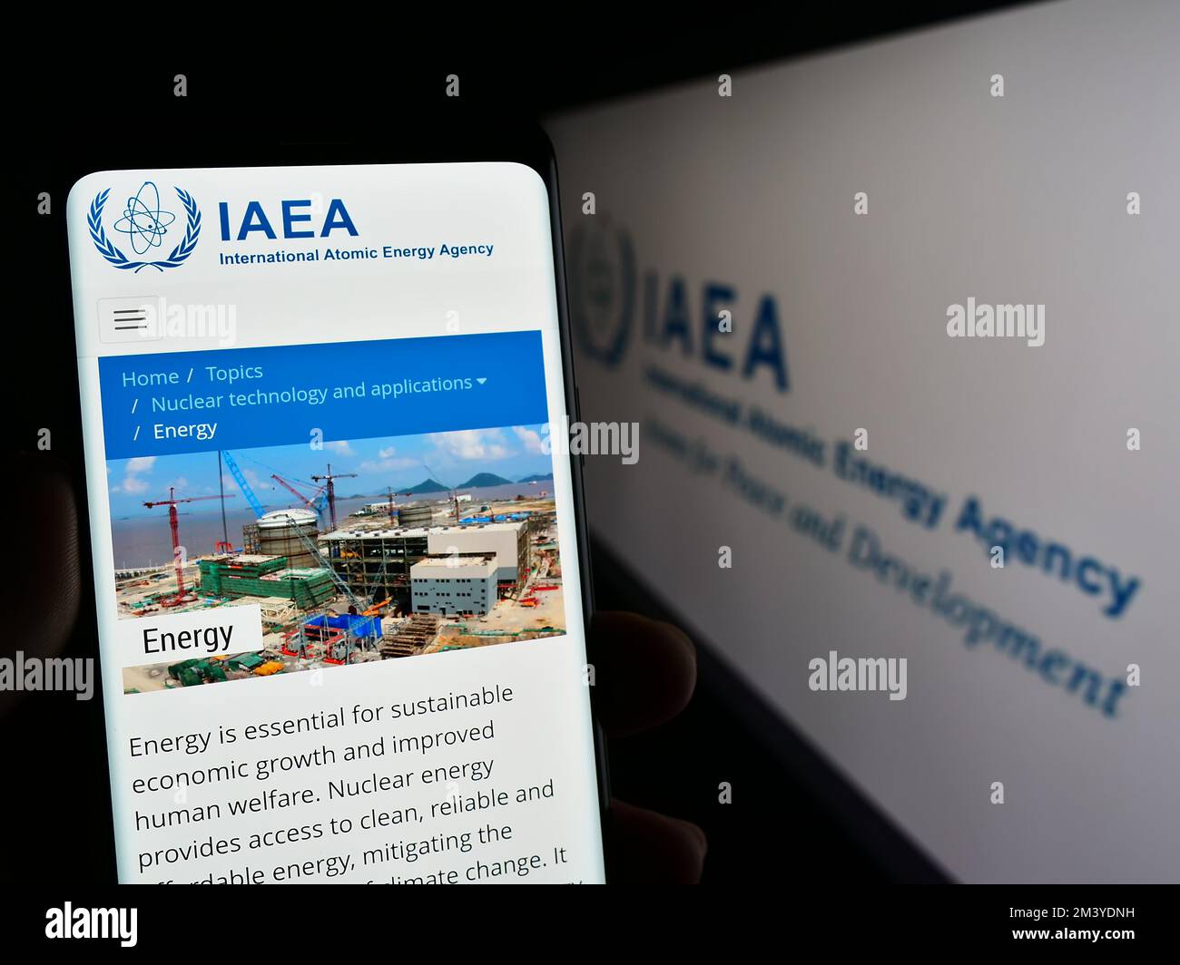 Persona che tiene il cellulare con la pagina web dell'Agenzia internazionale per l'energia atomica (AIEA) sullo schermo davanti al logo. Messa a fuoco al centro del display del telefono. Foto Stock