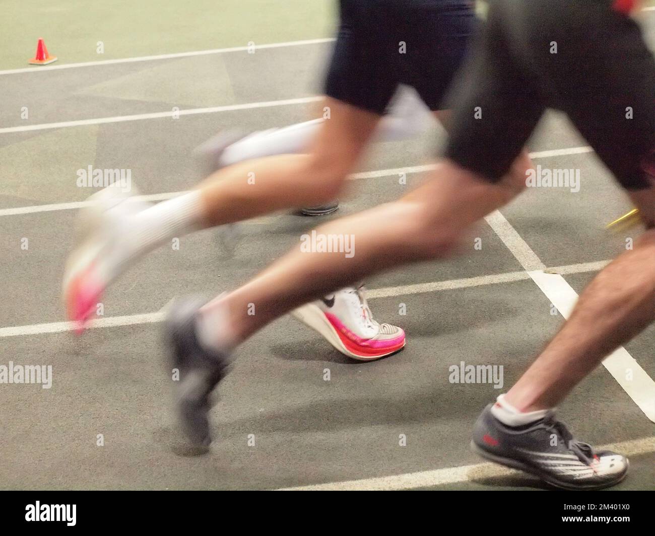 Le scarpe dei corridori sfocate all'inizio di una gara in un circuito indoor della High School del New Jersey si incontrano. Foto Stock