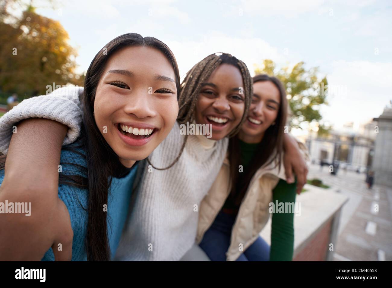 Gruppo di tre allegre amiche che guardano la telecamera abbracciandosi tra loro felici ragazze all'aperto Foto Stock