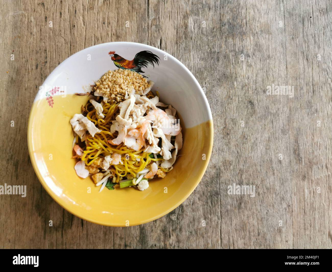 Spaghetti all'uovo giallo secco con gamberi e pollo a fette in una ciotola su sfondo di tavolo di legno. Cibo di strada asiatico, Thailandia. Foto Stock