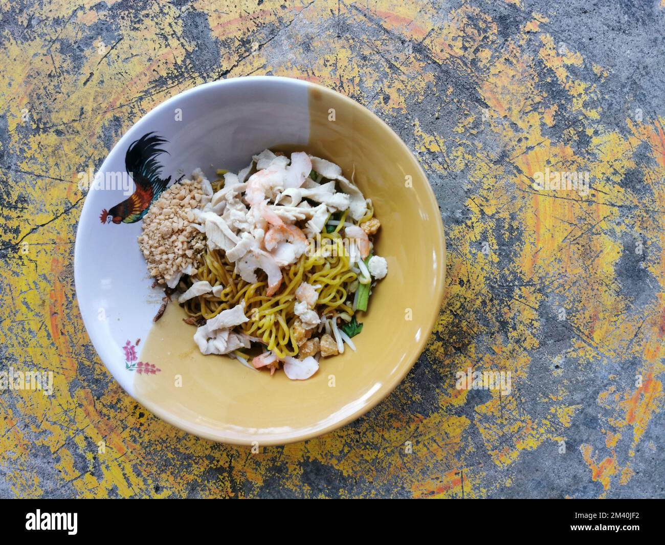 Spaghetti all'uovo giallo secco con gamberi e pollo a fette in una ciotola su fondo di cemento. Cibo di strada asiatico, Thailandia. Foto Stock