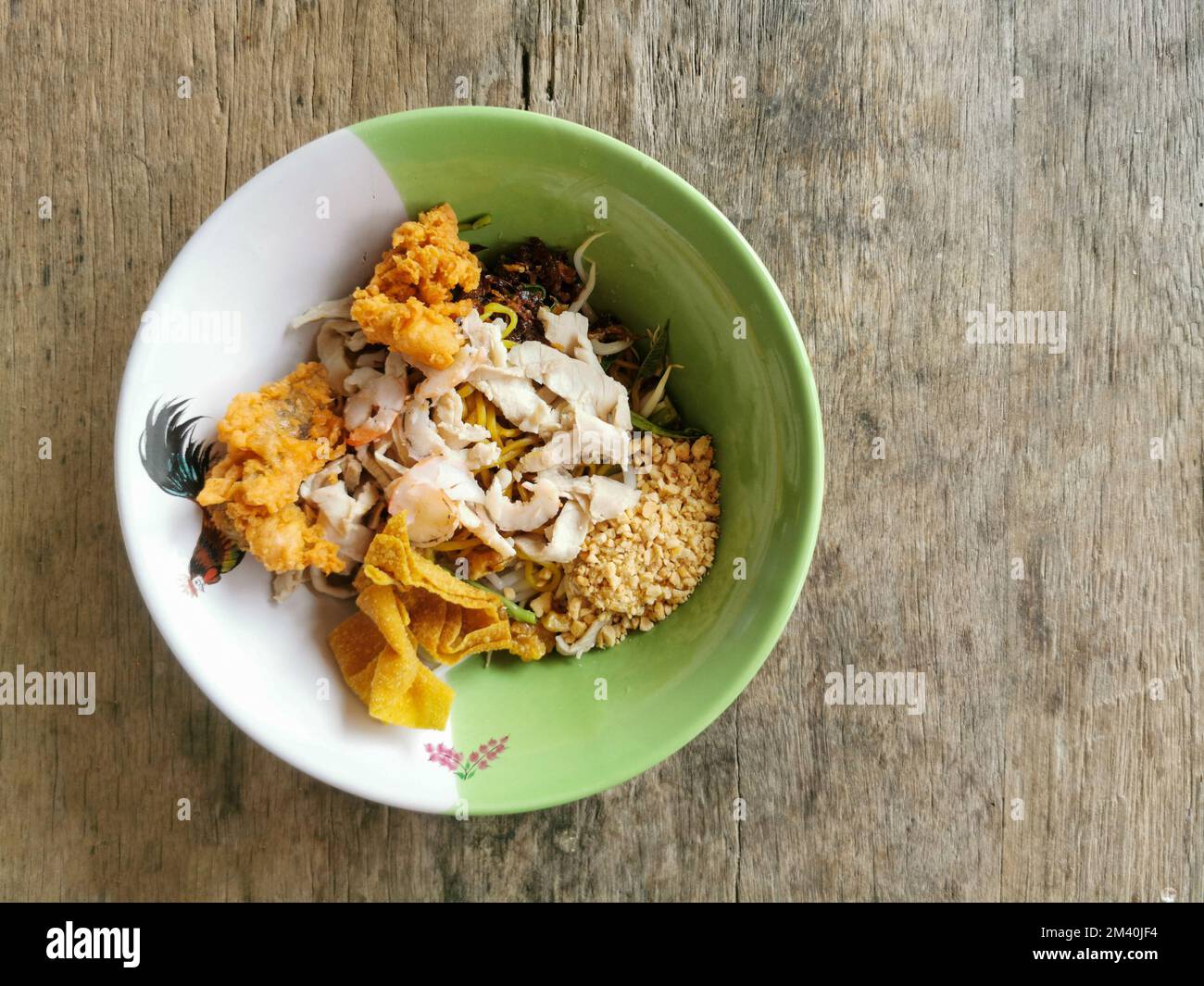 Spaghetti all'uovo giallo secco con gamberi, pollo a fette e wonton in una ciotola su sfondo tavolo di legno. Cibo di strada asiatico, Thailandia. Foto Stock