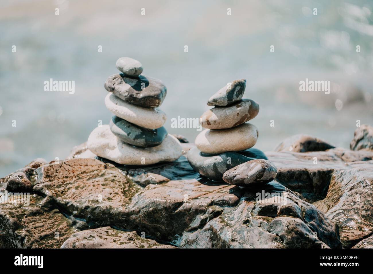 Piramide di roccia bilanciata sulla spiaggia di ciottoli, giorno di sole e cielo limpido al tramonto. Bokeh Golden Sea sullo sfondo. Fuoco selettivo, pietre zen sulla spiaggia di mare Foto Stock