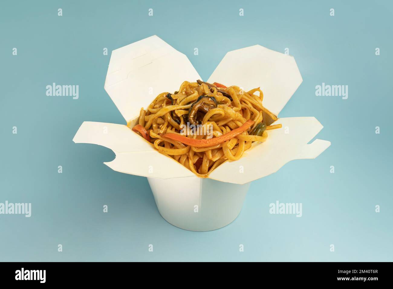 Tagliatelle Udon con pollo fritto, frutti di mare e verdure nella scatola di cartone con bacchette di legno sul colore di sfondo blu brillante. Foto Stock