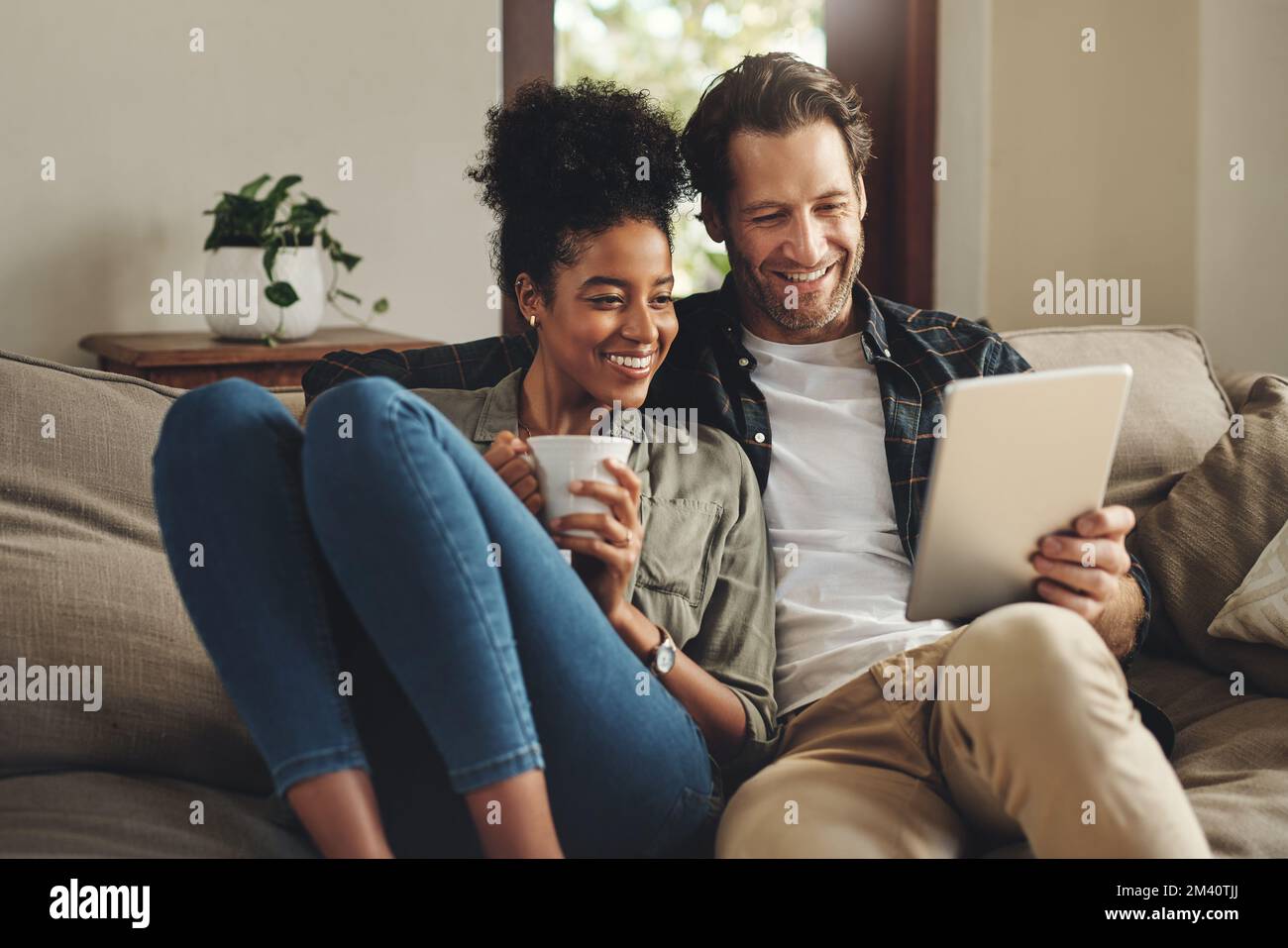 Queste app ci assicurano sempre un intrattenimento. una giovane coppia felice che usa un tablet digitale mentre si rilassa sul divano a casa. Foto Stock