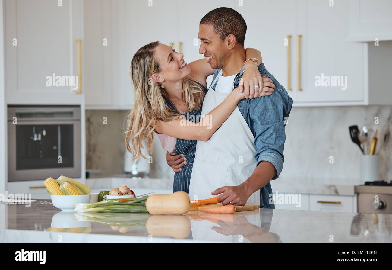 Cucina, amore o abbraccio di coppia in una cucina con dieta alimentare sana in un rapporto interrazziale o matrimonio a casa. Carota, verdure o donna felice Foto Stock