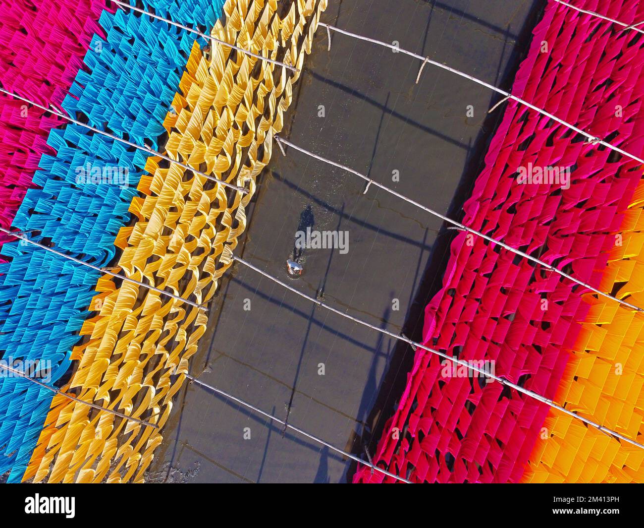 Narayanganj, Dhaka, Bangladesh. 18th Dec, 2022. Una scintillante rete di colori interconnessi produce un arcobaleno di colori mentre tessuti colorati vengono appesi ad asciugare sopra un campo allagato a Narayanganj, Bangladesh. I fili di ferro sono usati tra una struttura di bambù per generare le linee giganti di lavaggio per la parte finale del processo di tintura dopo che i panni sono fatti in t-shirt e giubbotti alla fabbrica dell'abbigliamento. Circa 4.000 pezzi di tessuto sono appesi ad asciugare qui ogni giorno. Il processo richiede solitamente cinque ore, con ogni set di 80 pezzi alla volta. Credit: ZUMA Press, Inc./Alamy Live News Foto Stock