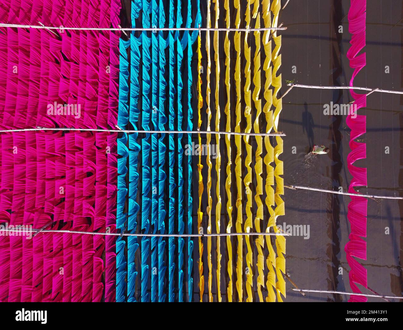 Narayanganj, Dhaka, Bangladesh. 18th Dec, 2022. Una scintillante rete di colori interconnessi produce un arcobaleno di colori mentre tessuti colorati vengono appesi ad asciugare sopra un campo allagato a Narayanganj, Bangladesh. I fili di ferro sono usati tra una struttura di bambù per generare le linee giganti di lavaggio per la parte finale del processo di tintura dopo che i panni sono fatti in t-shirt e giubbotti alla fabbrica dell'abbigliamento. Circa 4.000 pezzi di tessuto sono appesi ad asciugare qui ogni giorno. Il processo richiede solitamente cinque ore, con ogni set di 80 pezzi alla volta. Credit: ZUMA Press, Inc./Alamy Live News Foto Stock