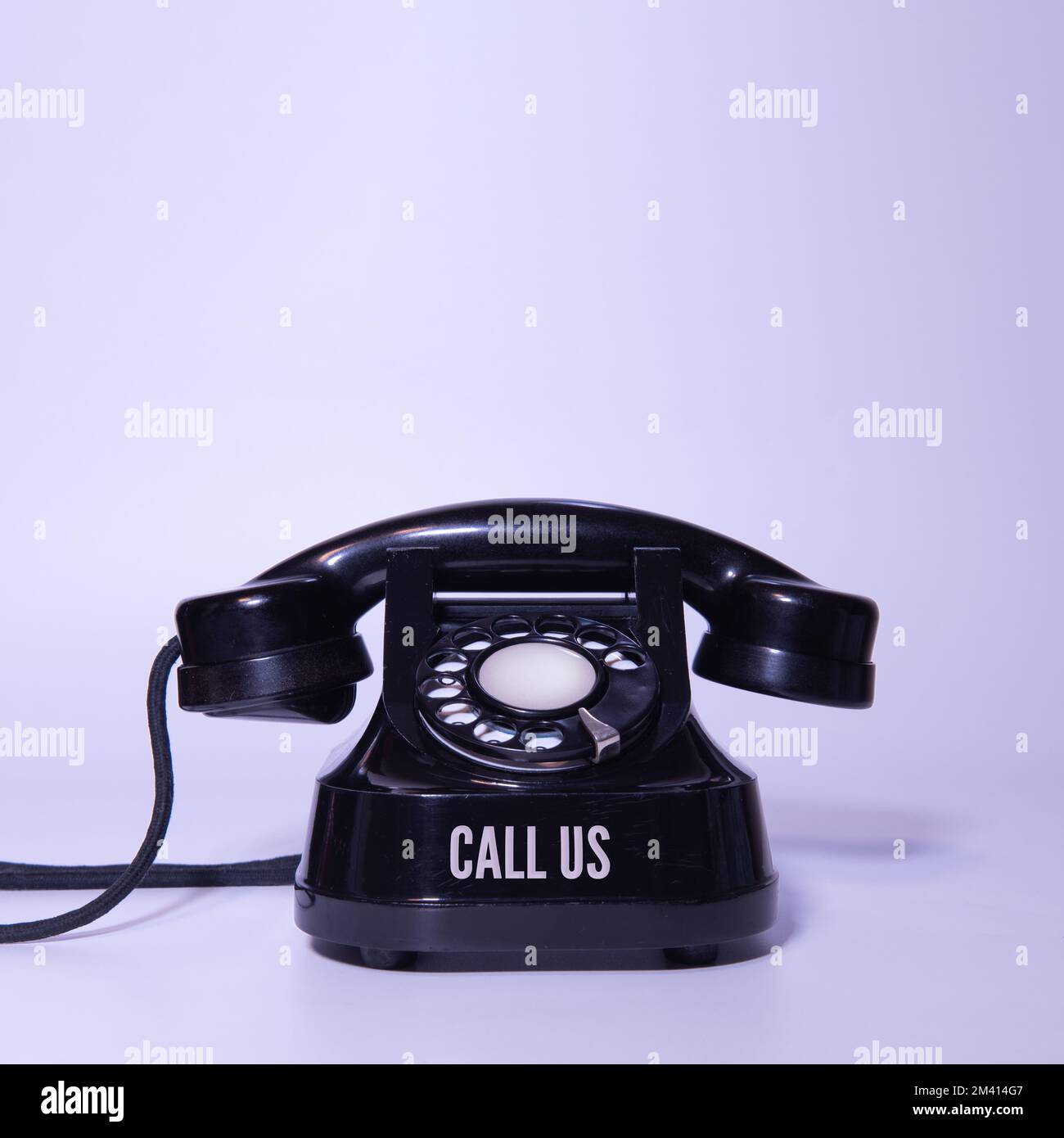 Vecchio telefono nero su sfondo viola chiaro. con un'iscrizione - chiamaci Foto Stock